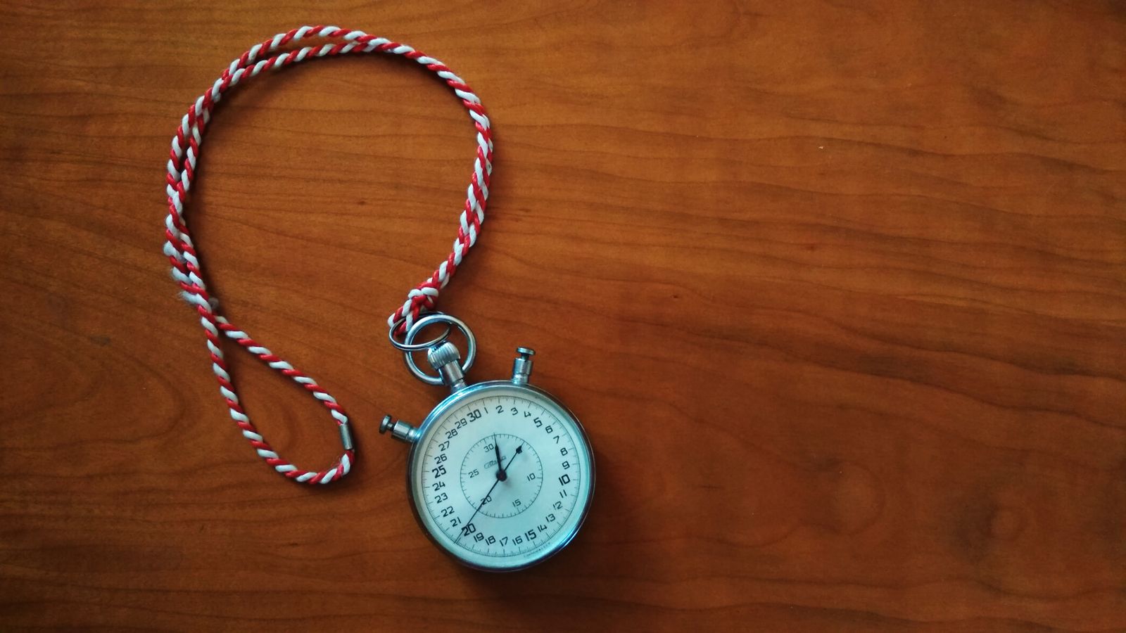 Round silver colored analog stopwatch on brown wooden panel