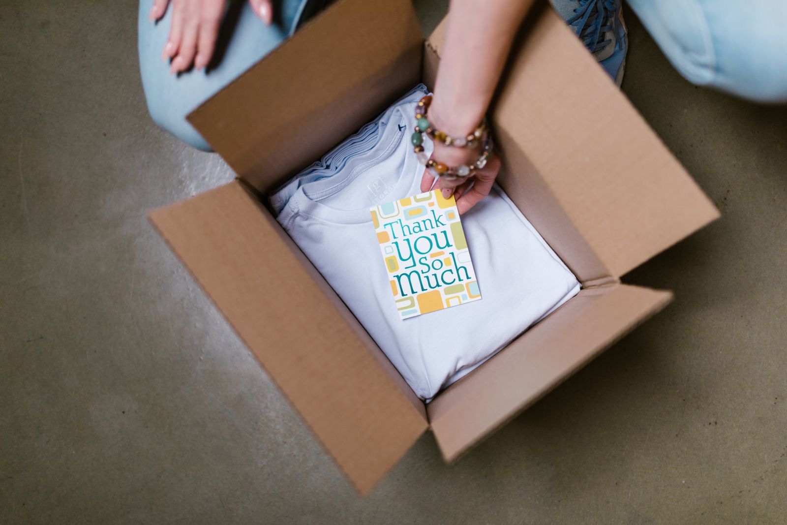 Woman putting thank you card into box with t shirts