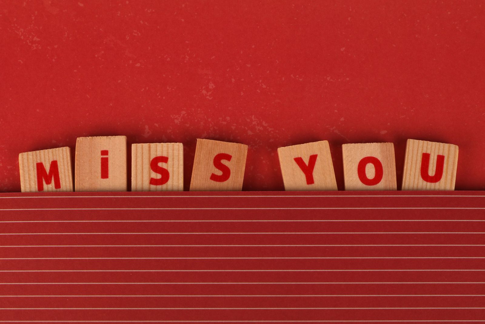 Wooden blocks spelling miss you on red background